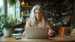 © svastix - A gray-haired woman concentrates on her laptop in a cozy kitchen filled with natural light, evoking an aura of calmness, focus, and modern-day comfort.