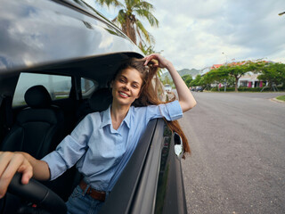 Woman driving car with head out window, hair blowing in wind; joyful expression, sunny weather, casual attire, scenic landscape passing by; captures freedom, adventure, carefree spirit