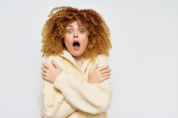 Poster - Surprised young woman with curly hair in a cozy sweater, expressing shock against a light background, embodying surprise and emotion in a playful, engaging manner