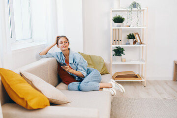 Happy Woman Holding Mobile Phone on Cozy Sofa in Living Room, Enjoying Online Game and Chatting in Cyberspace