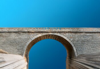 Aufkleber - A stone archway stands against a bright blue sky, with the edges of the bridge leading into the distance.