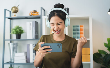 Excited Young Asian woman wearing headset and playing online game on smartphone.