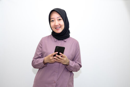 Portrait of emotional Asian, Indonesian woman wearing purple shirt and hijab headscarf laughing and holding handphone. Isolated on white background