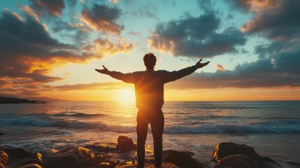 Wall Mural - a man stands on a beach with his arms outstretched, looking up at the sky