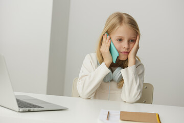 Smiling girl learning at home with her laptop a modern education concept in the digital age The cute Caucasian schoolgirl is sitting at a table, wearing headphones, typing on her notebook, fully