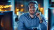 © Anoo - Happy customer service agent in call center at night wearing a headset, smiling while assisting clients at his computer workstation