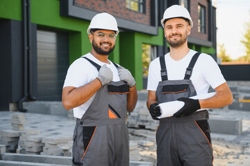 Two builders or architects checking the construction plan against the background of new cottages