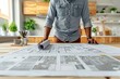 © TesaI - Man examining blueprints on wooden table. Modern kitchen background. Natural light. Focus on planning and design. Casual attire suggests home renovation project