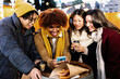 © Xavier Lorenzo - Young multiracial group of friends in winter clothes using mobile phone outdoor during christmas holidays.