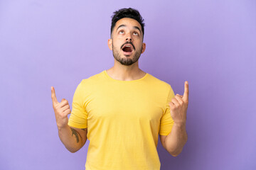 Young caucasian man isolated on purple background surprised and pointing up