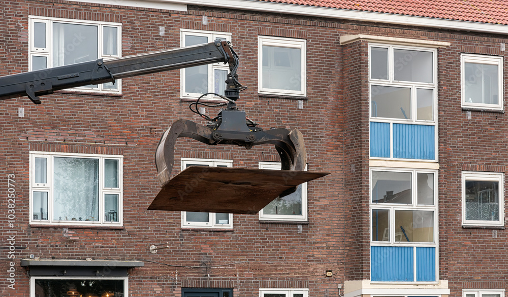 steel plate is lifted by a pneumatic steel grabber hanging from an industrial crane