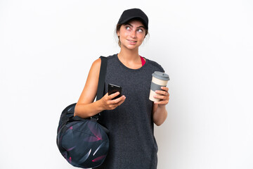 Young sport woman with sport bag isolated on white background holding coffee to take away and a mobile while thinking something