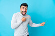 © luismolinero - Caucasian man over isolated blue background surprised and pointing side