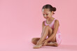 © New Africa - Little ballerina putting on pointe shoes against pink background, space for text