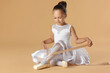 © New Africa - Little ballerina tying pointe shoes on beige background