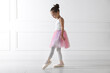 © New Africa - Little ballerina practicing dance moves near white wall indoors