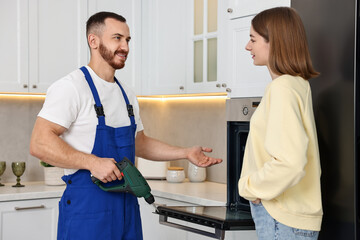 Poster - Smiling repairman with drill consulting woman near oven in kitchen