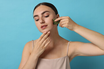 Poster - Beautiful young woman doing facial massage with gua sha tool on light blue background