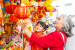 © CandyRetriever  - Happy Asian family grandmother and grandchild girl in red Chinese clothing choosing and buying home decorative ornaments for celebration Chinese Lunar New Year holiday festival at Chinatown market.