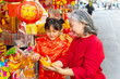 © CandyRetriever  - Happy Asian family grandmother and grandchild girl in red Chinese clothing choosing and buying home decorative ornaments for celebration Chinese Lunar New Year holiday festival at Chinatown market.