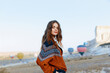 © VICHIZH - Woman in sweater and pants standing in front of hot air balloon in desert landscape