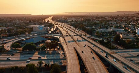 Wall Mural - Setting sun lights the multi-lane highways of interchange in Los Angeles, California, US. Drone footage above the roads with numerous cars.