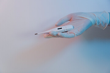 The doctor's hand in the medical glove holding a thermometer, isolated on the white-blue background with copy space. 