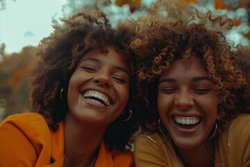 Portrait of two joyful young women with curly hair laughing together in a close-up shot, exuding happiness and friendship in a warm autumn setting with vibrant colorsfriends