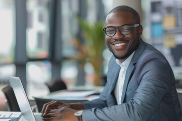 Happy businessman smiling with tablet, phone, and laptop inside the modern office.