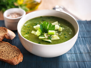 A colorful bowl of detox soup featuring spinach, zucchini, and celery, topped with parsley and served with bread ai.