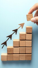 A hand places a block on a staircase of cubes, illustrating growth with upward arrows against a soft blue background.