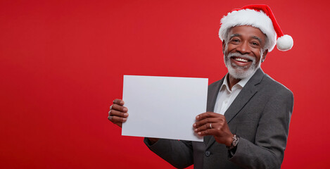 Elderly African American man in business suit and Santa hat holding blank white sign on red background