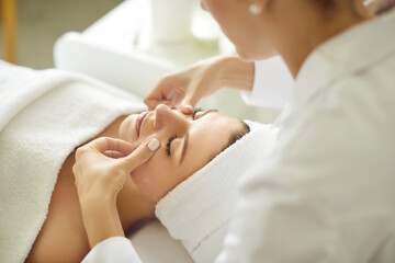 Wall Mural - Close up portrait of a beautiful young woman lying with closed eyes and having face or head massage in spa. Woman relax enjoying health therapy treatment. Wellness and beauty day concept.