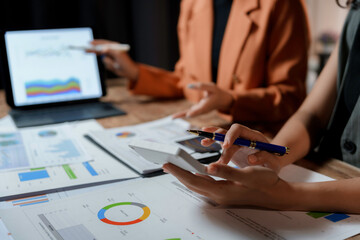 Business team working with financial data, calculating and analyzing graphs on paperwork and digital tablet during a meeting