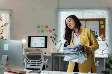 Asian businesswoman is smiling while carrying a stack of paperwork in a modern office