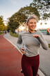 © Zamrznuti tonovi - Young sporty woman running in the park listening music and smiling