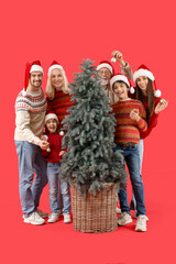 Wall Mural - Big family in Santa hats decorating Christmas tree on red background