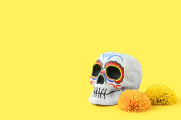 Painted skull for Mexico's Day of the Dead (El Dia de Muertos) and marigold flowers on yellow background