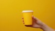 © Kharkovich - Hand holding a yellow coffee cup against a plain yellow background