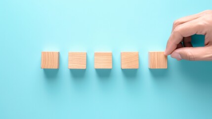 A hand adjusts one of five wooden blocks on a light blue surface during a creative activity or brainstorming session