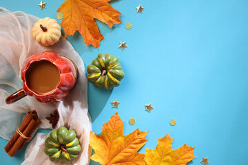 Wall Mural - Autumn flat lay composition with scarf, cup of coffee, maple leaves, pumpkins, cinnamon sticks on blue background. Autumn, Fall, Thanksgiving concept.