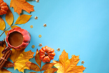 Wall Mural - Autumn composition. Frame made of yellow leaves, cup of coffee, cinnamon sticks, pumpkins on blue background . Autumn concept. Flat lay, top view, copy space