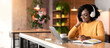 © Prostock-studio - Happy black girl in wireless headphones studying online, using laptop and taking notes, cafe interior, copy space