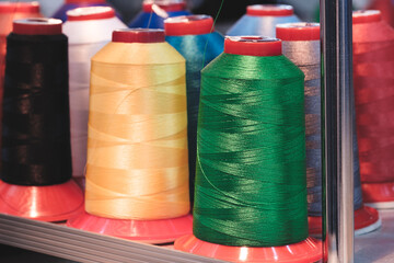 Aufkleber - A rack of colorful spools of thread. The spools are of different colors and sizes. The spools are arranged in a row, with the green one in the middle