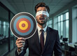 © Gianpiero - A businessman in a suit stands blindfolded, holding a target. The image captures themes of risk, challenge, and uncertainty in a corporate environment.