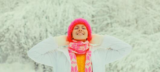 Wall Mural - Happy cheerful smiling young woman in colorful knitted hat, enjoys weather in winter snowy park