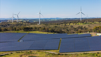 Wall Mural - aerial drone view of a hybrid solar and wind farm showing the large wind turbines in the background 