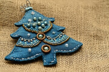 Wall Mural - Handmade blue textile cotton fabric naive retro style Christmas tree ornament decorated with beads on burlap background, copy space background - generative ai