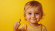 © The Stock Photo Girl - A cheerful toddler gives a thumbs-up against a bright yellow background.