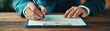 © Katawut - A person writes on a blank document using a pen, showcasing a focus on detail and professionalism in a warm, wooden office environment.